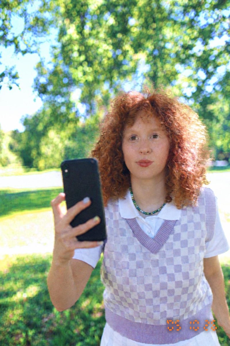 AI-generated: 2000s Date Stamp AI filter result: woman in a checkered vest holding a smartphone outdoors
