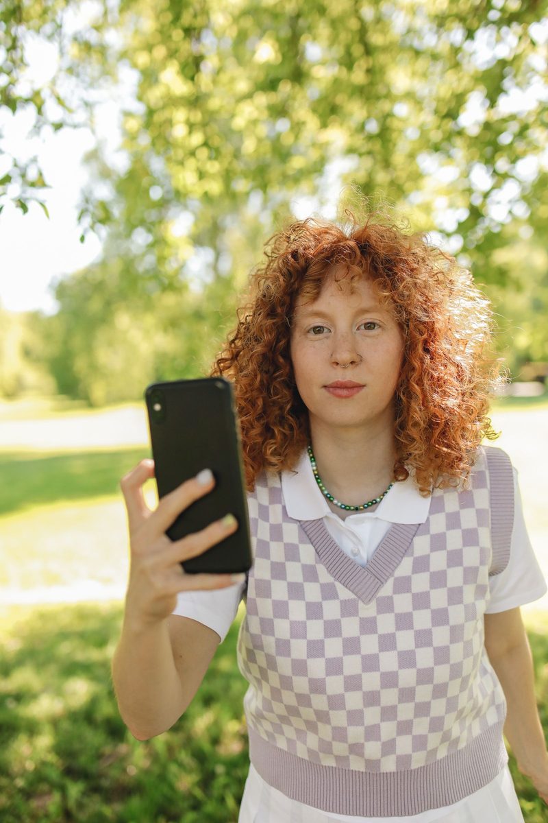 Before: 2000s Date Stamp AI filter result: woman in a checkered vest holding a smartphone outdoors