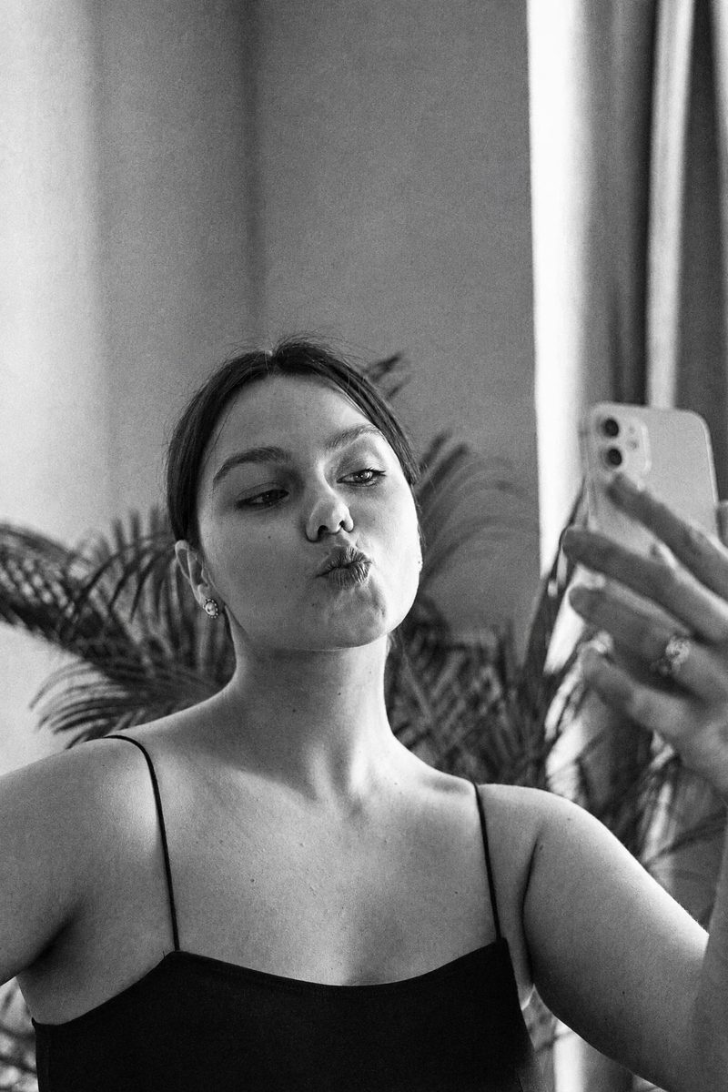AI-generated: Classic B&W Film AI filter result: woman in a black top taking a mirror selfie