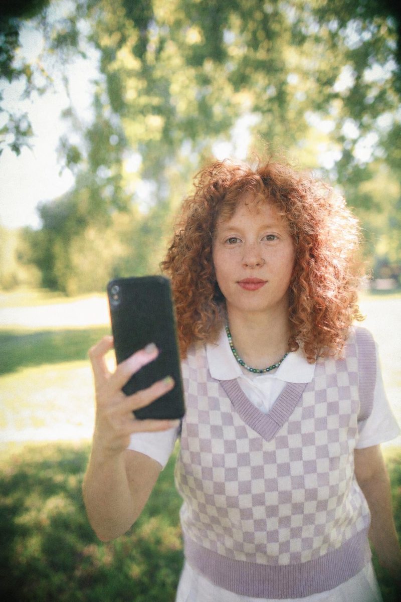 AI-generated: Disposable Camera AI filter result: woman in a checkered vest holding a smartphone outdoors