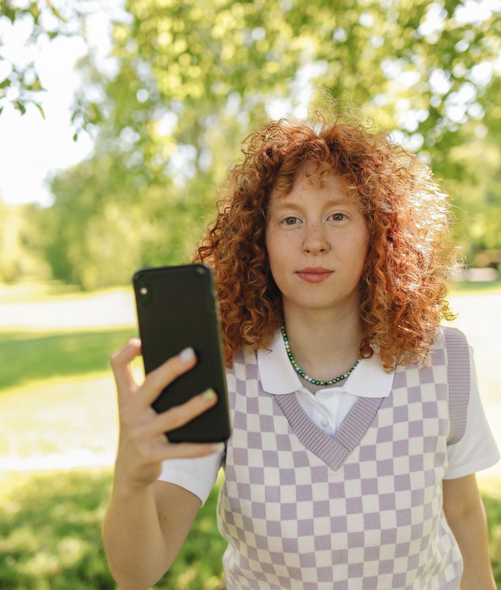 Before: Instant Film Frame AI filter result: woman in a checkered vest holding a smartphone outdoors
