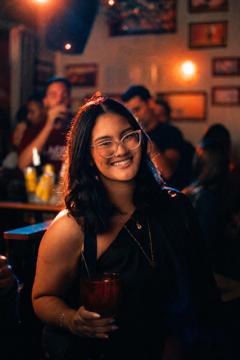 AI-generated: Night Tungsten 800 AI filter result: smiling woman with a drink on a night out at a bar