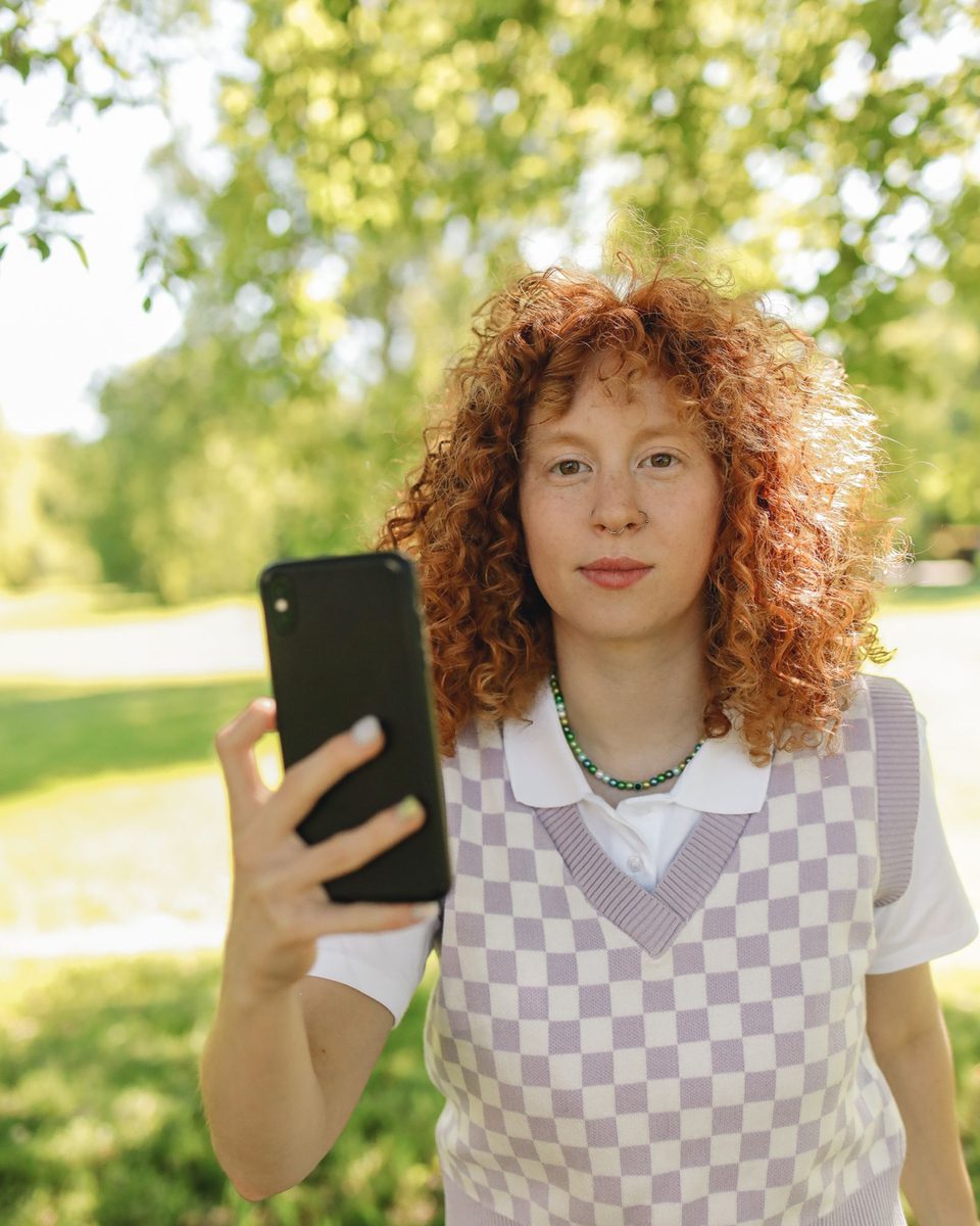 Before: Photobooth Strip AI filter result: woman in a checkered vest holding a smartphone outdoors