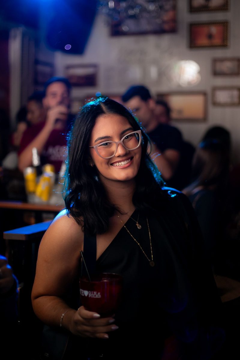 Before: Warm Portrait 400 AI filter result: smiling woman with a drink on a night out at a bar
